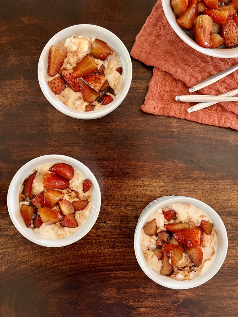Three ramikens with vanilla ice cream topped with balsamic vinegar strawberries with a bowl of more strawberries in the corner.